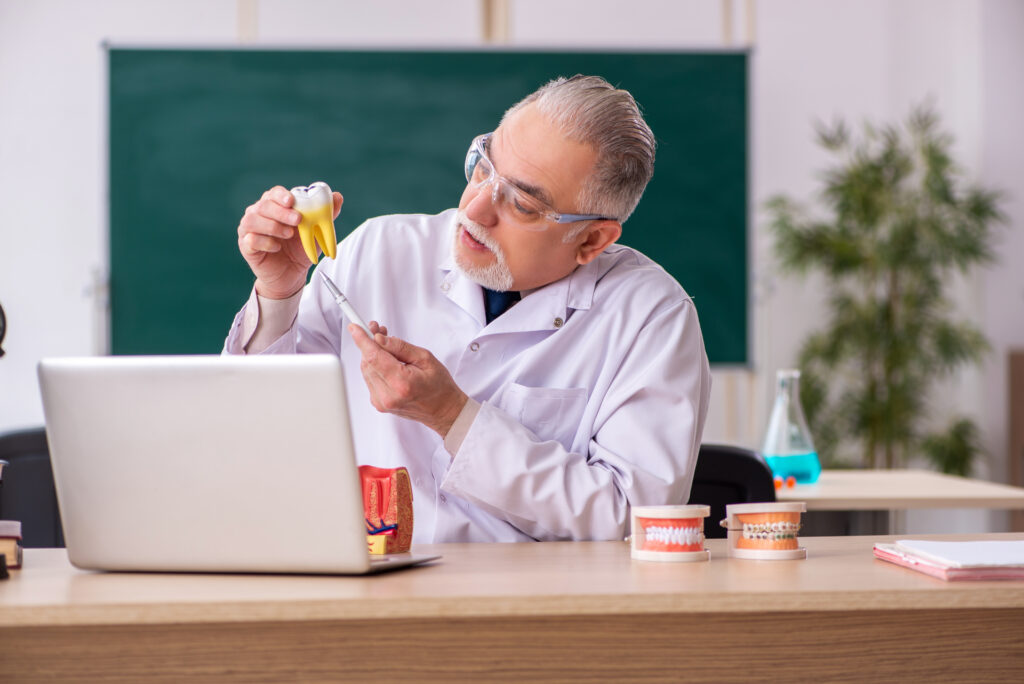 A man in a lab coat is administering dental care through his laptop.