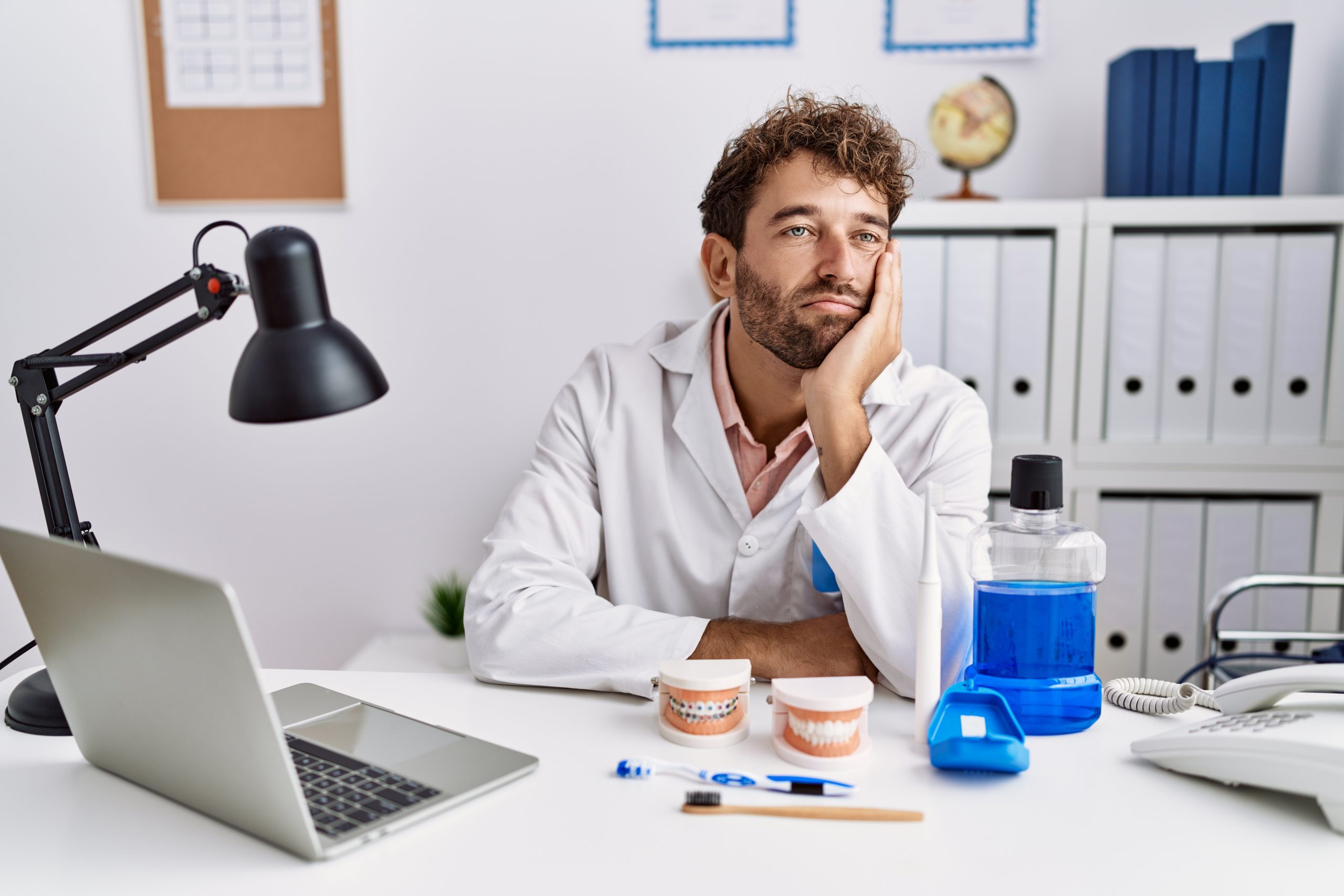 Burnt out dentist in office resting his chin on his hand.